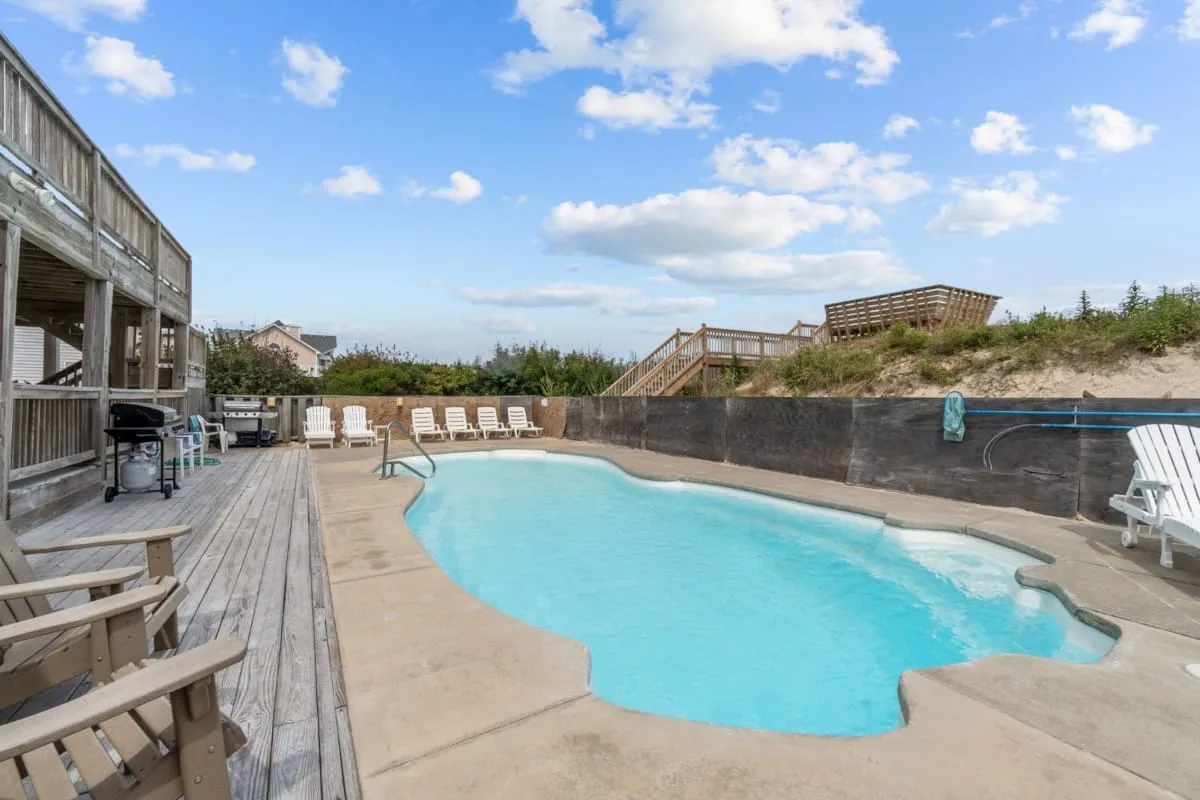 Una piscina al aire libre junto a una terraza de madera, con asientos alrededor.