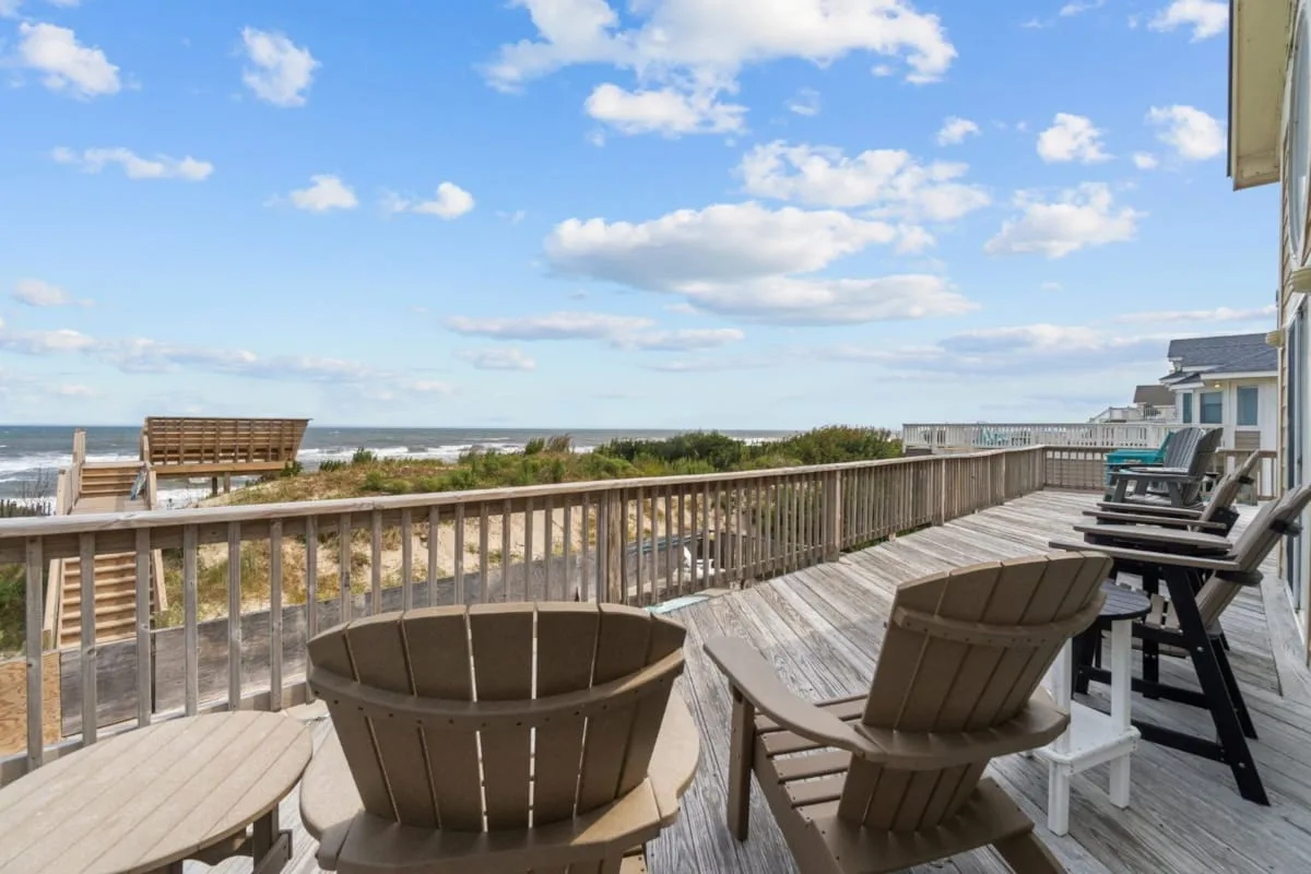 Una terraza de madera da a la playa, con asientos al aire libre y vista al océano.