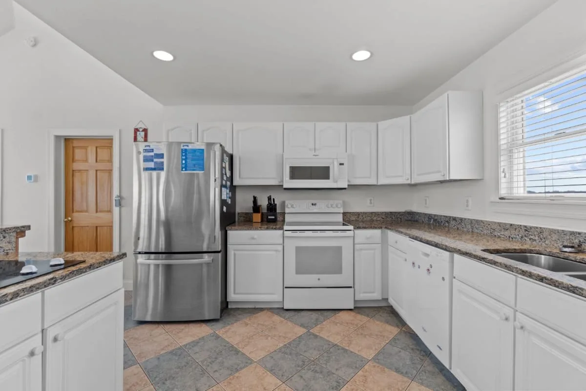 Una cocina luminosa con gabinetes blancos, electrodomésticos de acero inoxidable y piso de baldosas.