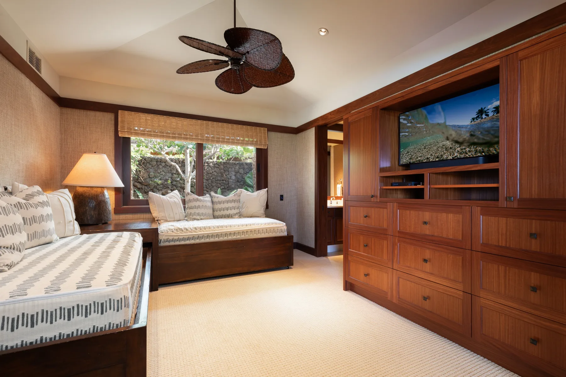 A bedroom with two beds and a wooden entertainment cabinet beneath a television.