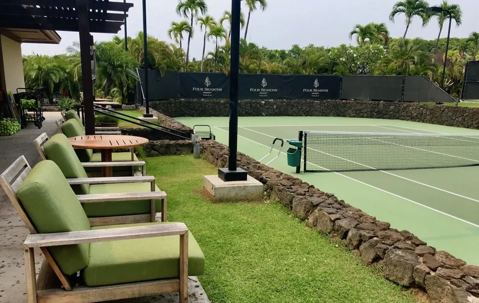 Outdoor tennis court with a net beside a grassy seating area.