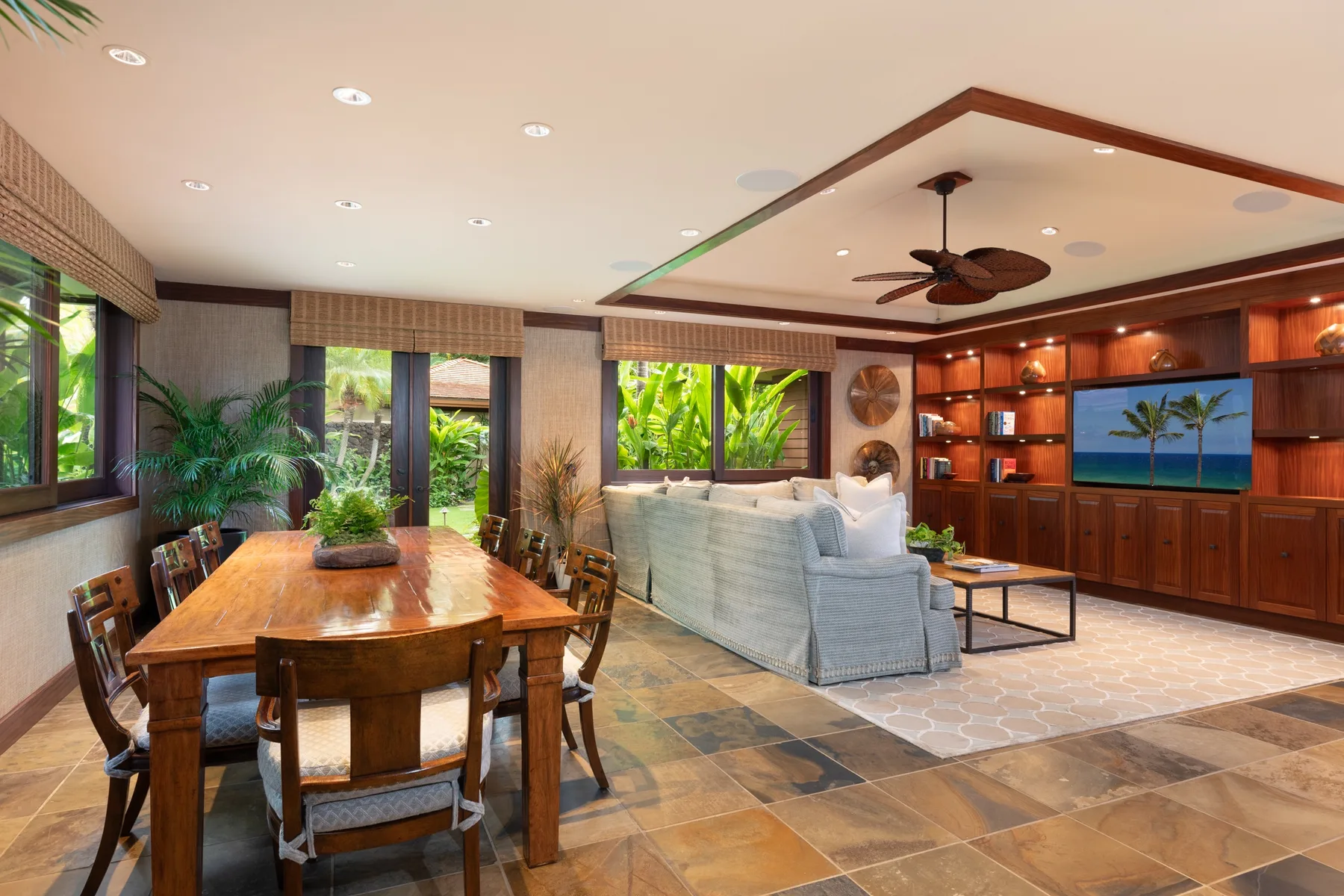 A living and dining area with seating, a wooden dining table, and large windows.
