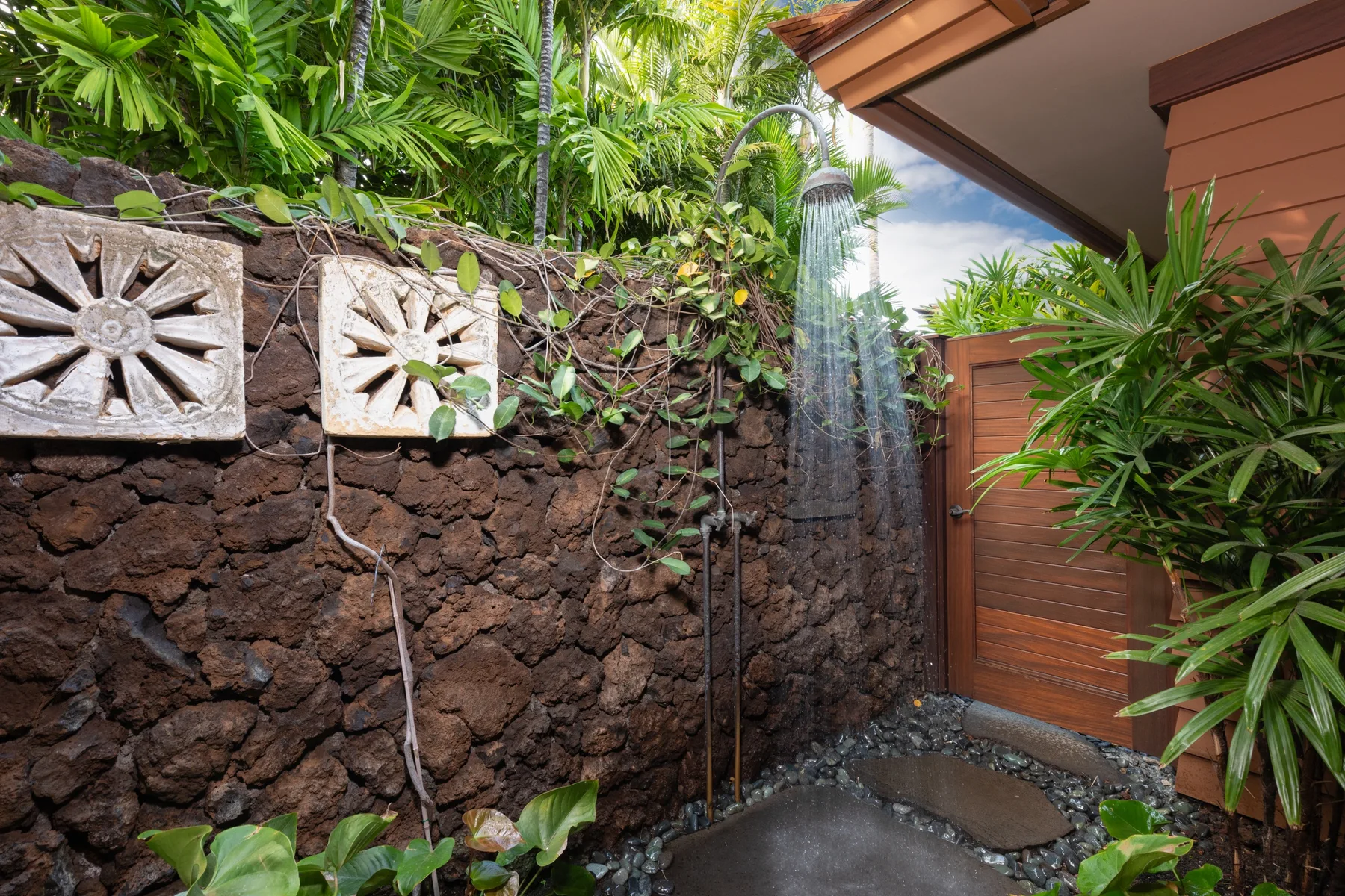 An outdoor shower stands beside a stone wall and wooden panel.