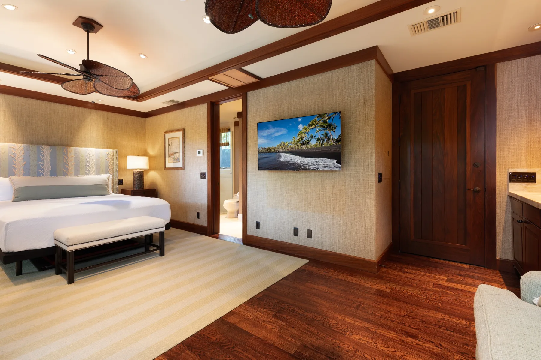 A bedroom with a bed, a wall-mounted television, and wooden flooring.