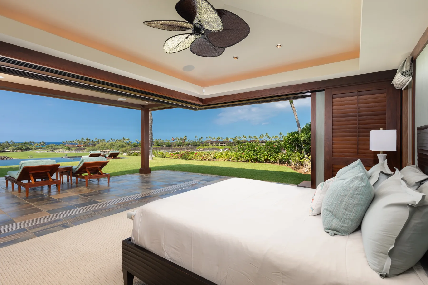 A bedroom opens onto a patio with outdoor seating and a view of the water.