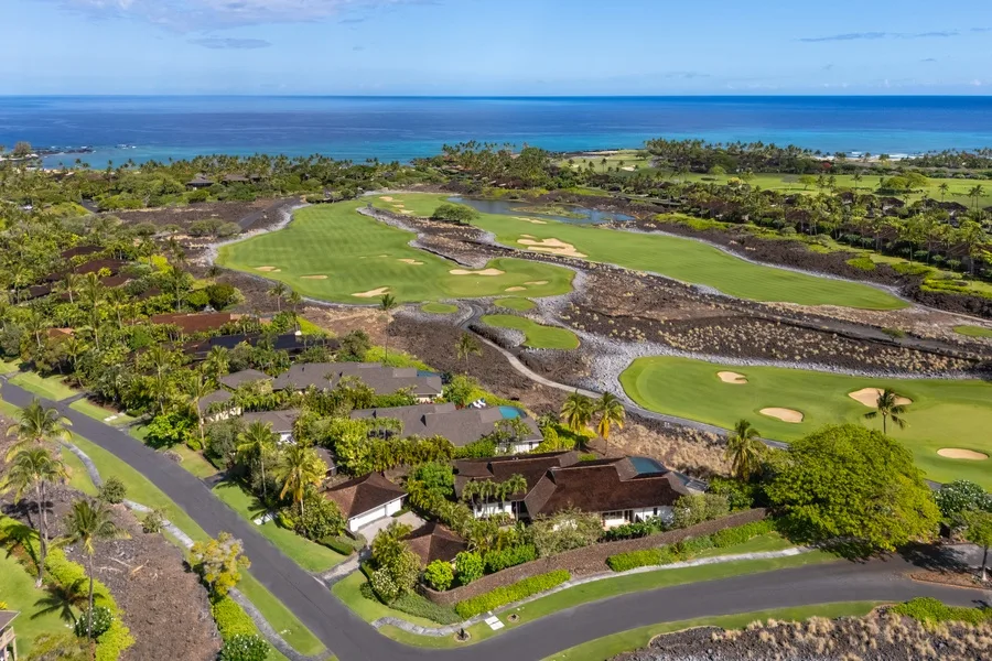 Aerial view of a coastal golf course with greens, roads, and the ocean beyond.