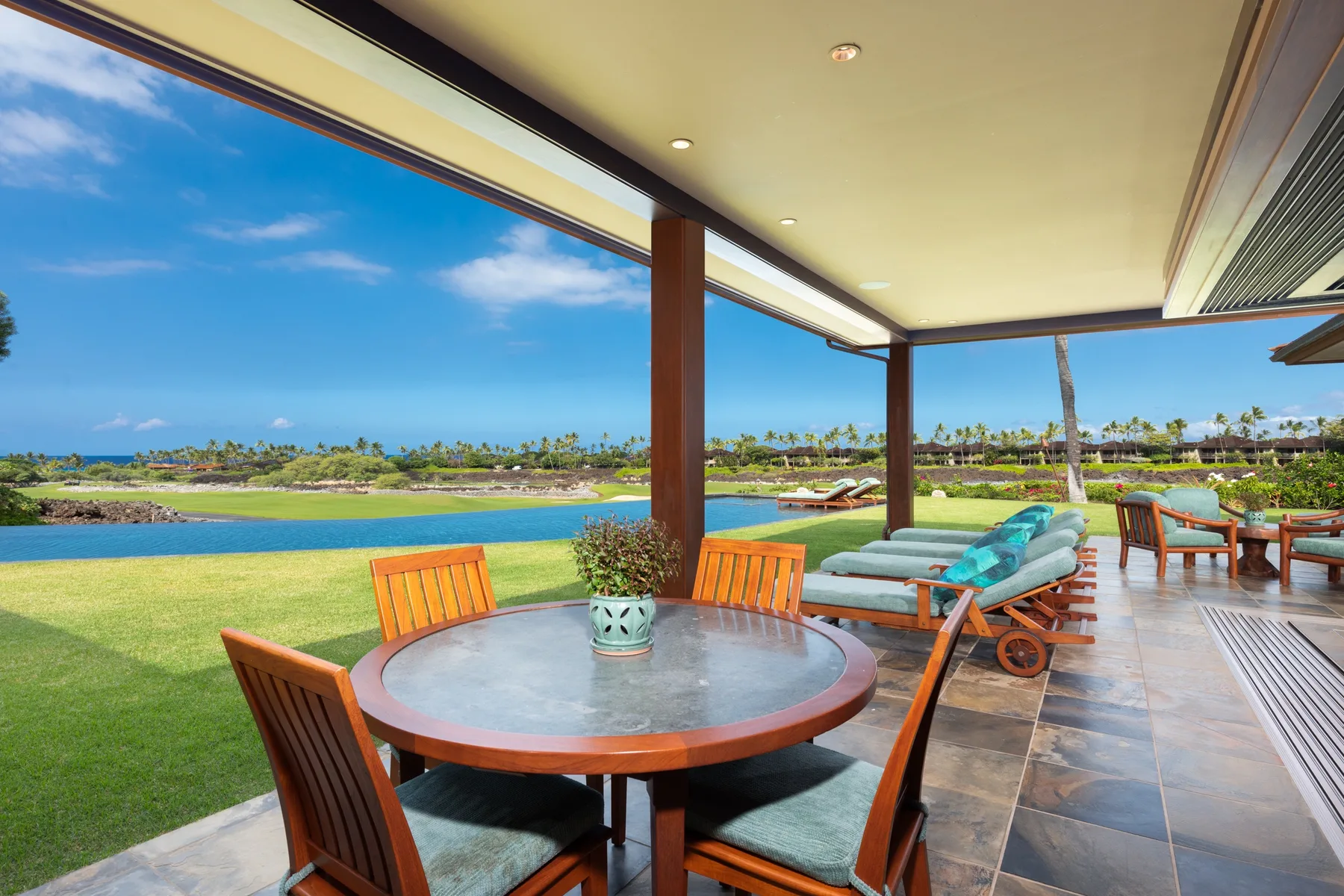 A covered patio with a round table and seating overlooks a lawn and water.