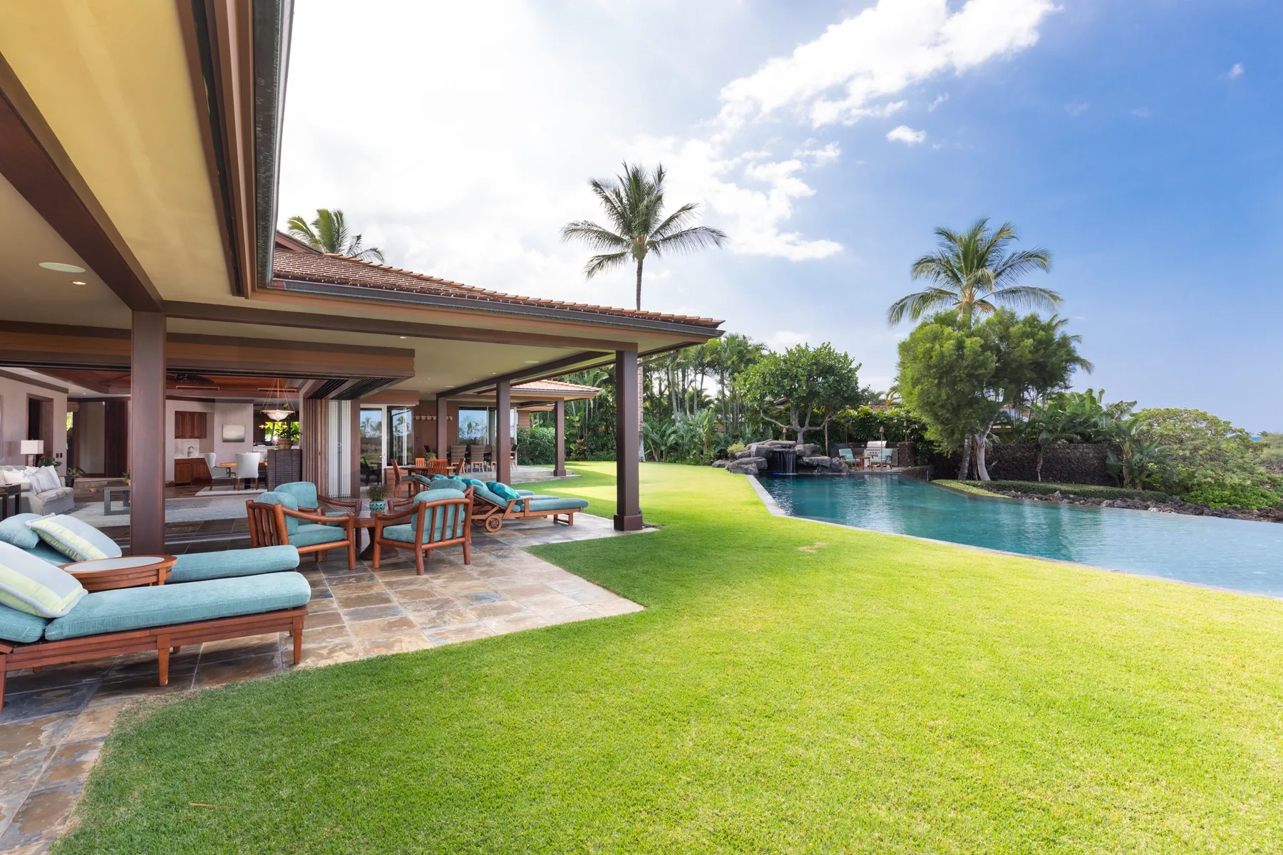 An outdoor patio with seating overlooks a lawn and swimming pool.