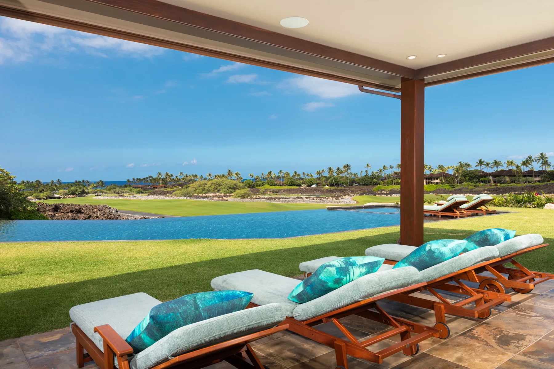 A covered outdoor seating area overlooks a lawn, water, and distant palm trees.