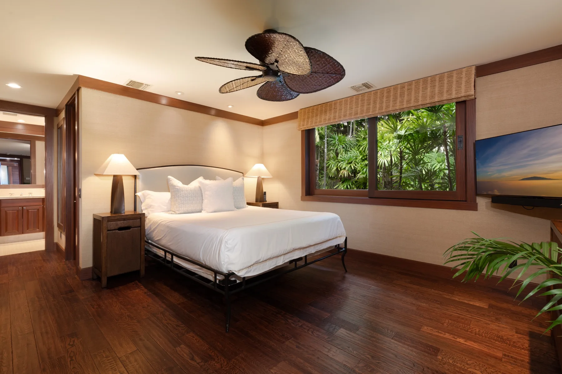 A bedroom with a bed, bedside lamps, and a window overlooking greenery.
