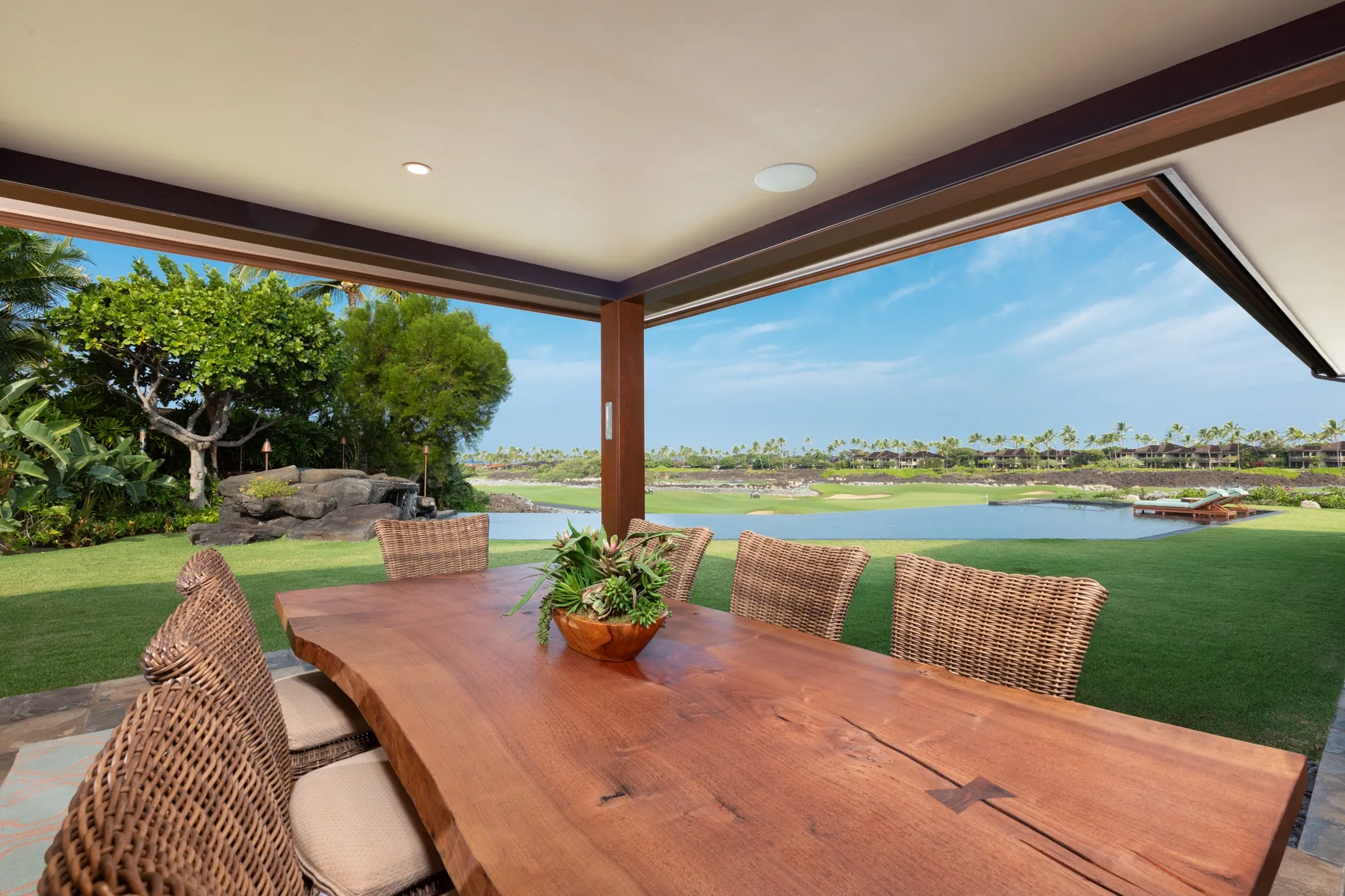 A covered patio dining area overlooks a lawn and a lake.