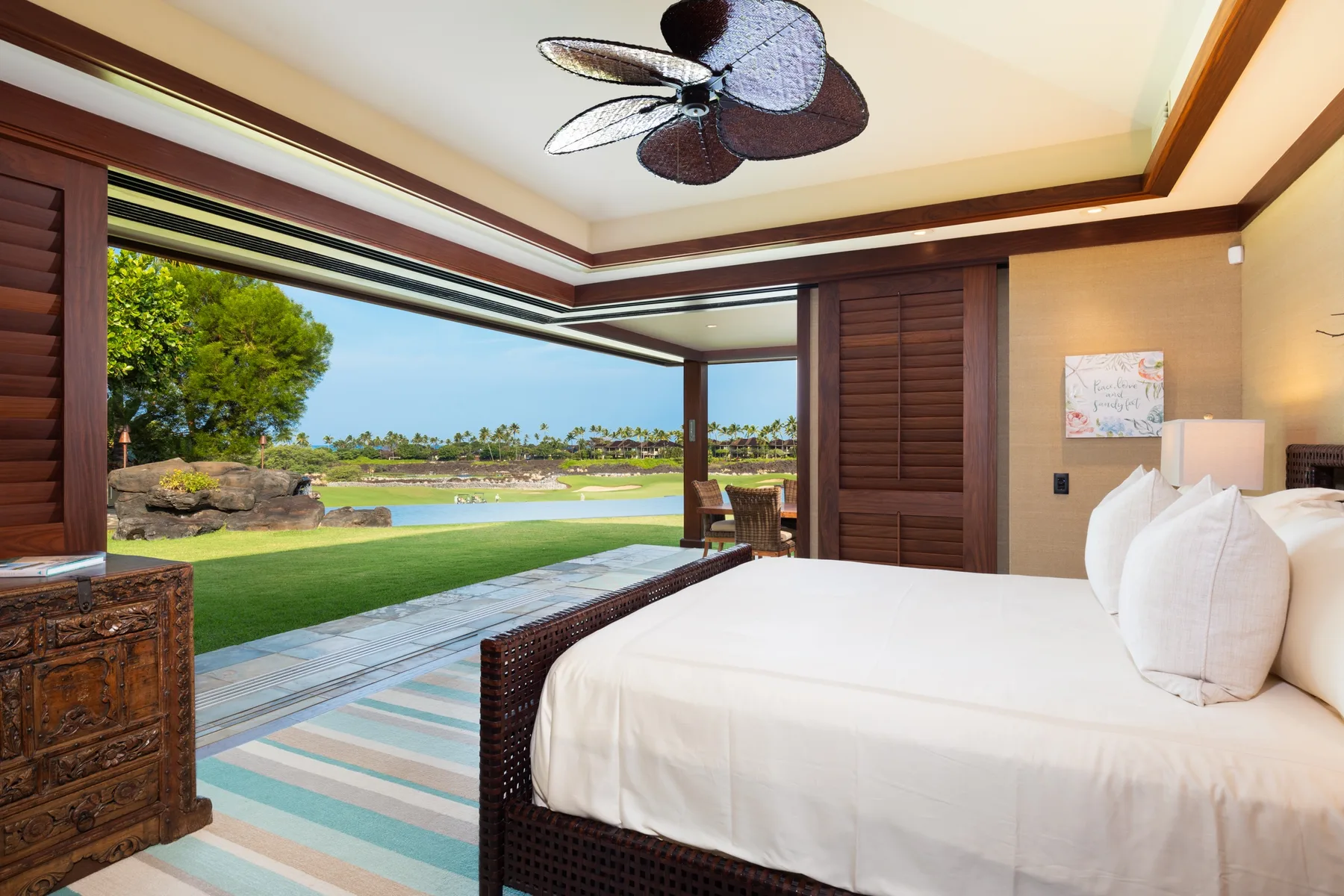 A bedroom opens onto a patio with a view of green grounds and water.