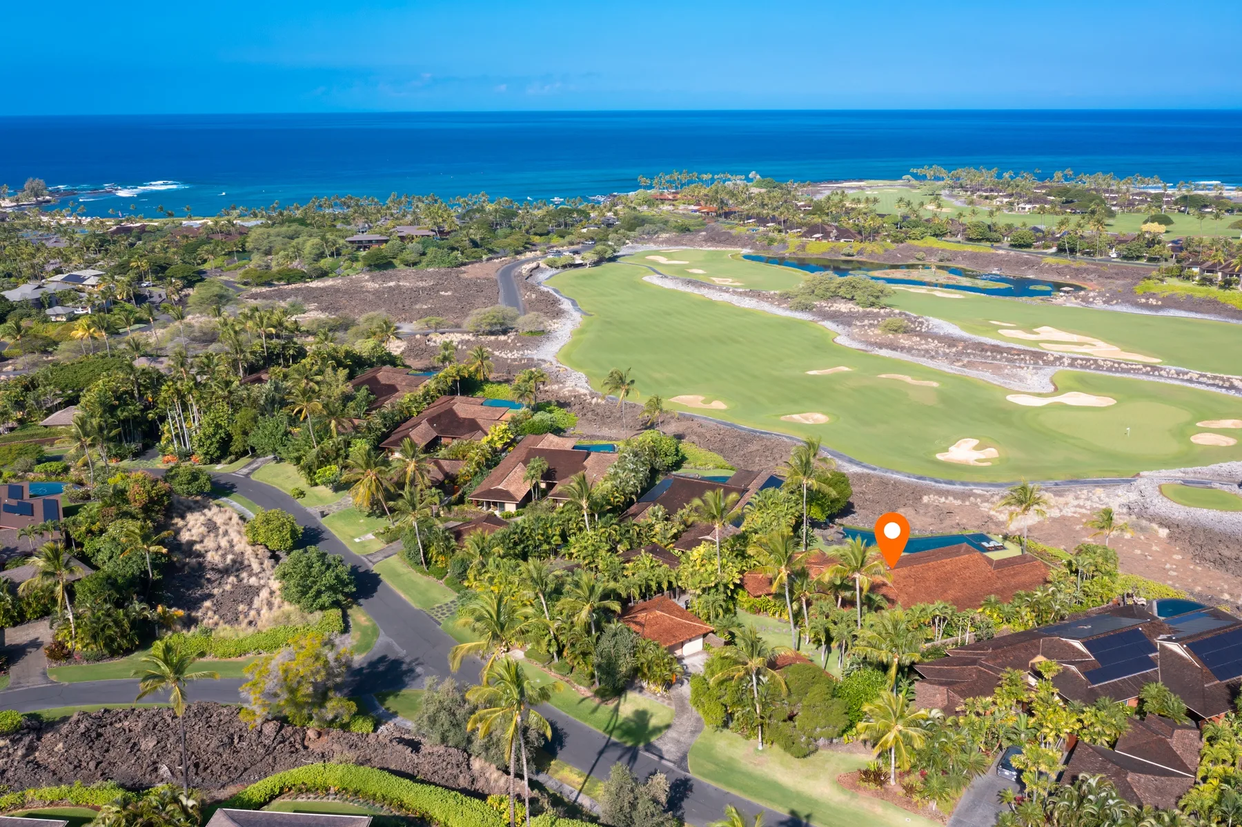 Aerial view of a coastal golf course, with homes and ocean beyond.