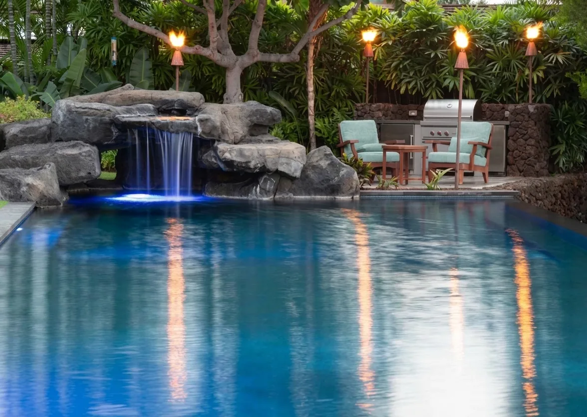 A swimming pool with a rock waterfall and a small seating area.