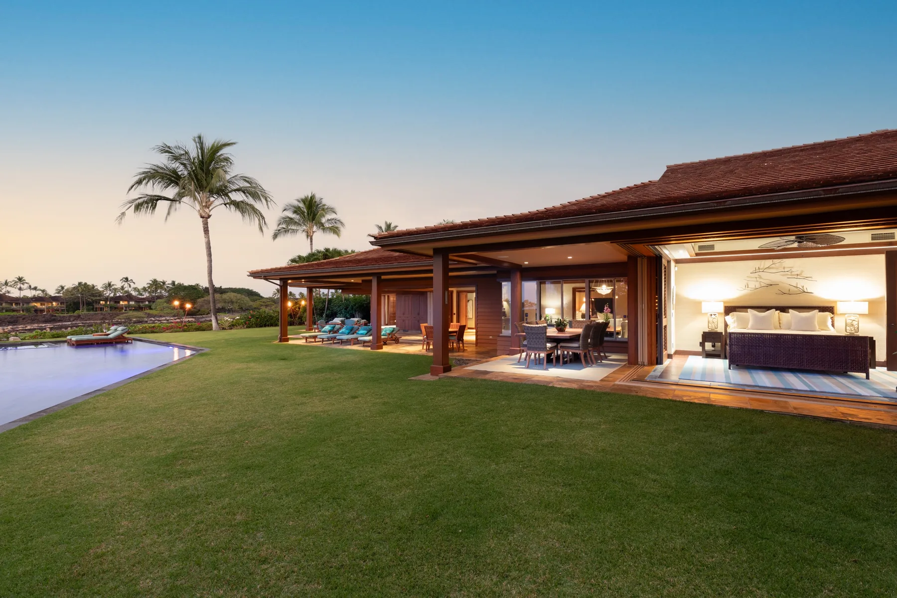A landscaped lawn borders a pool and an open-sided house at dusk.