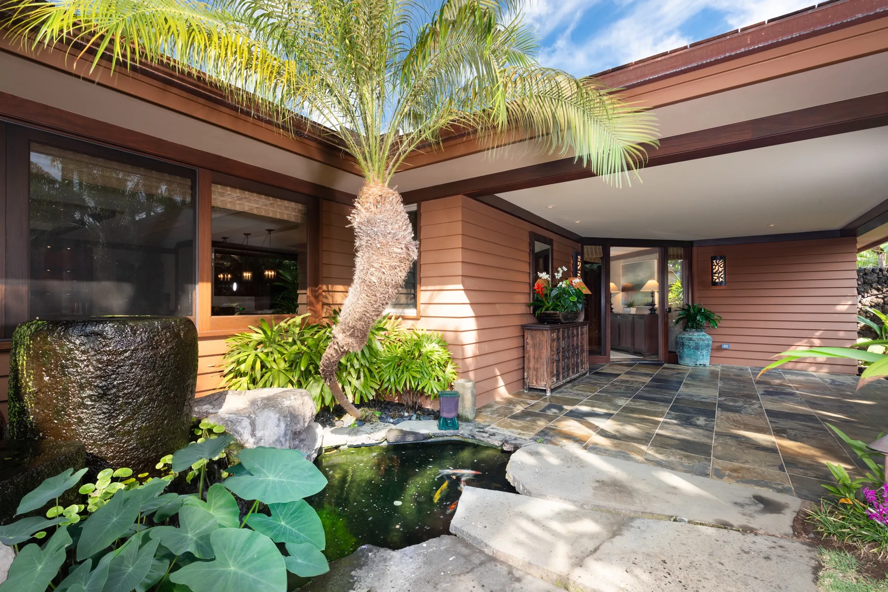 A covered patio with a tiled floor, tropical plants, and a small pond.