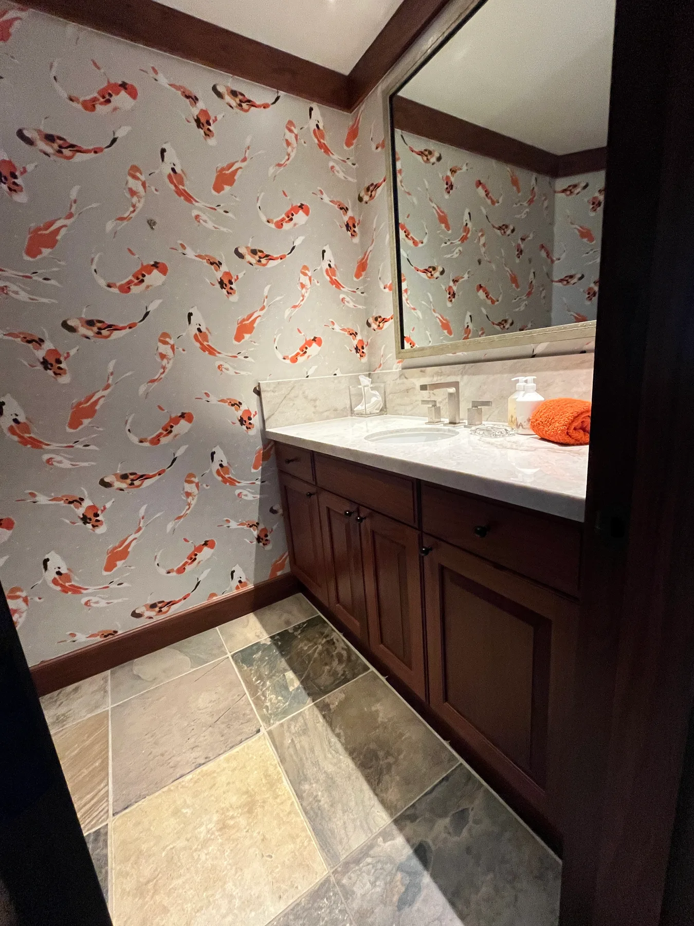 A bathroom vanity with a sink and mirror stands against fish-patterned wallpaper.