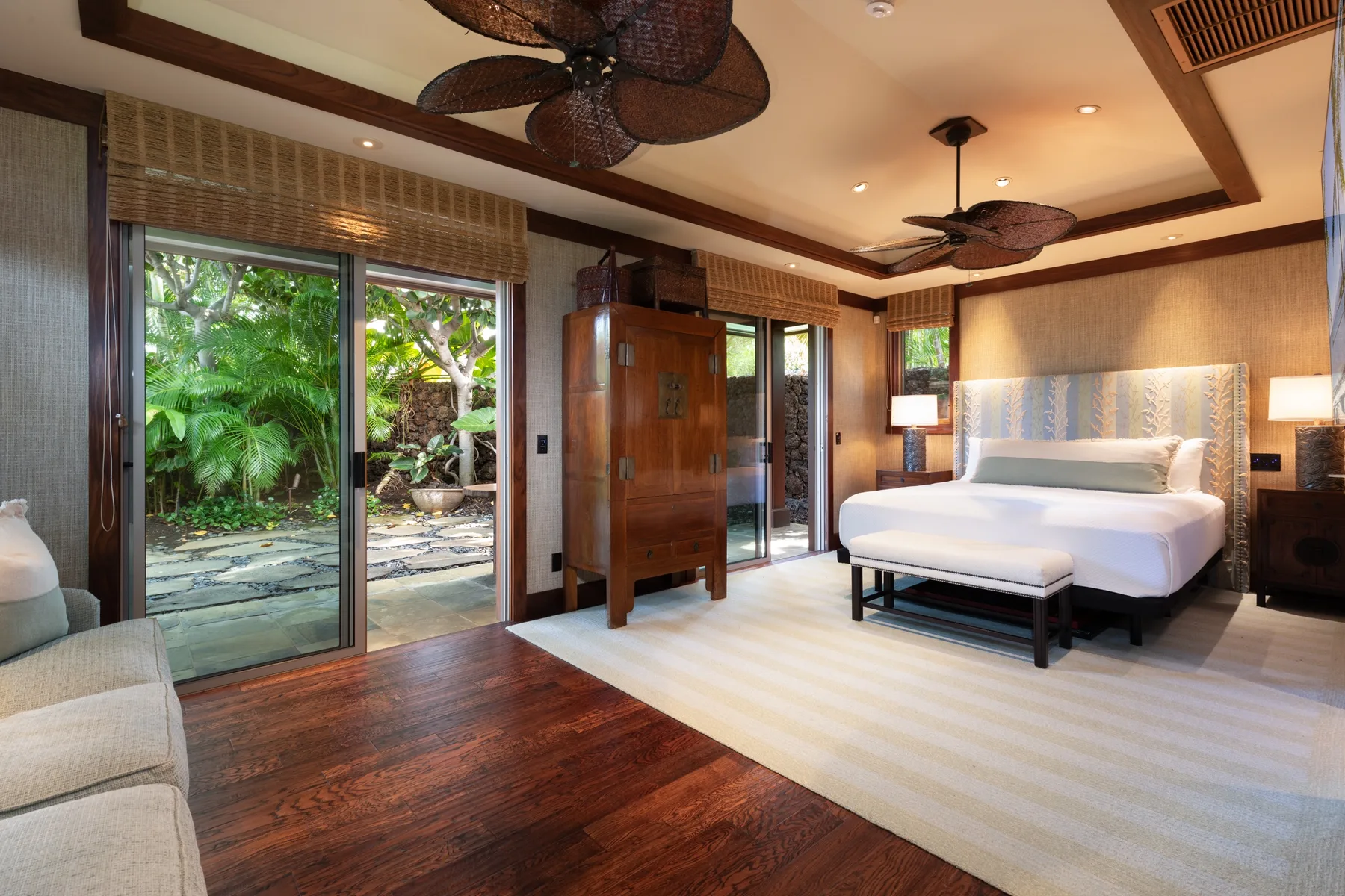 A bedroom with a large bed, a rug, and glass doors opening to greenery.