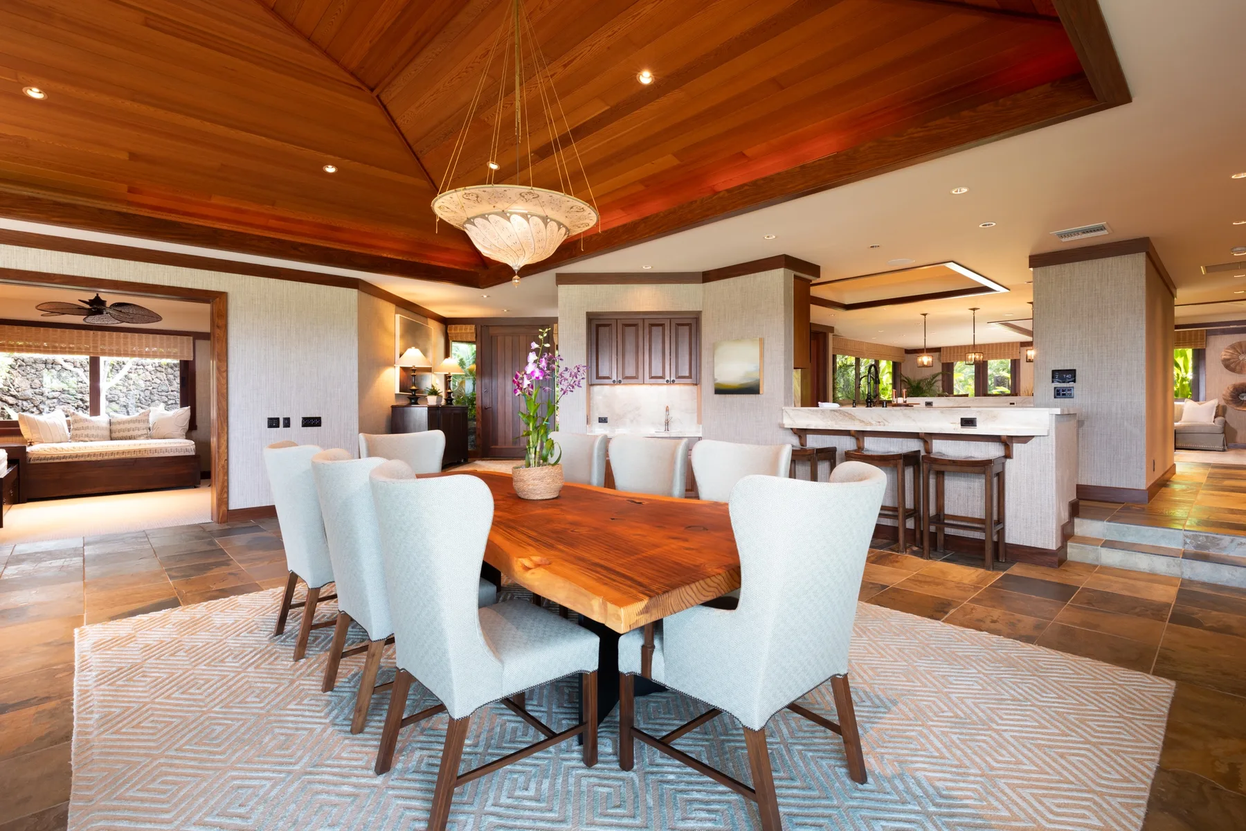 A dining area with a wooden table and light-colored seating beneath a wood-paneled ceiling.