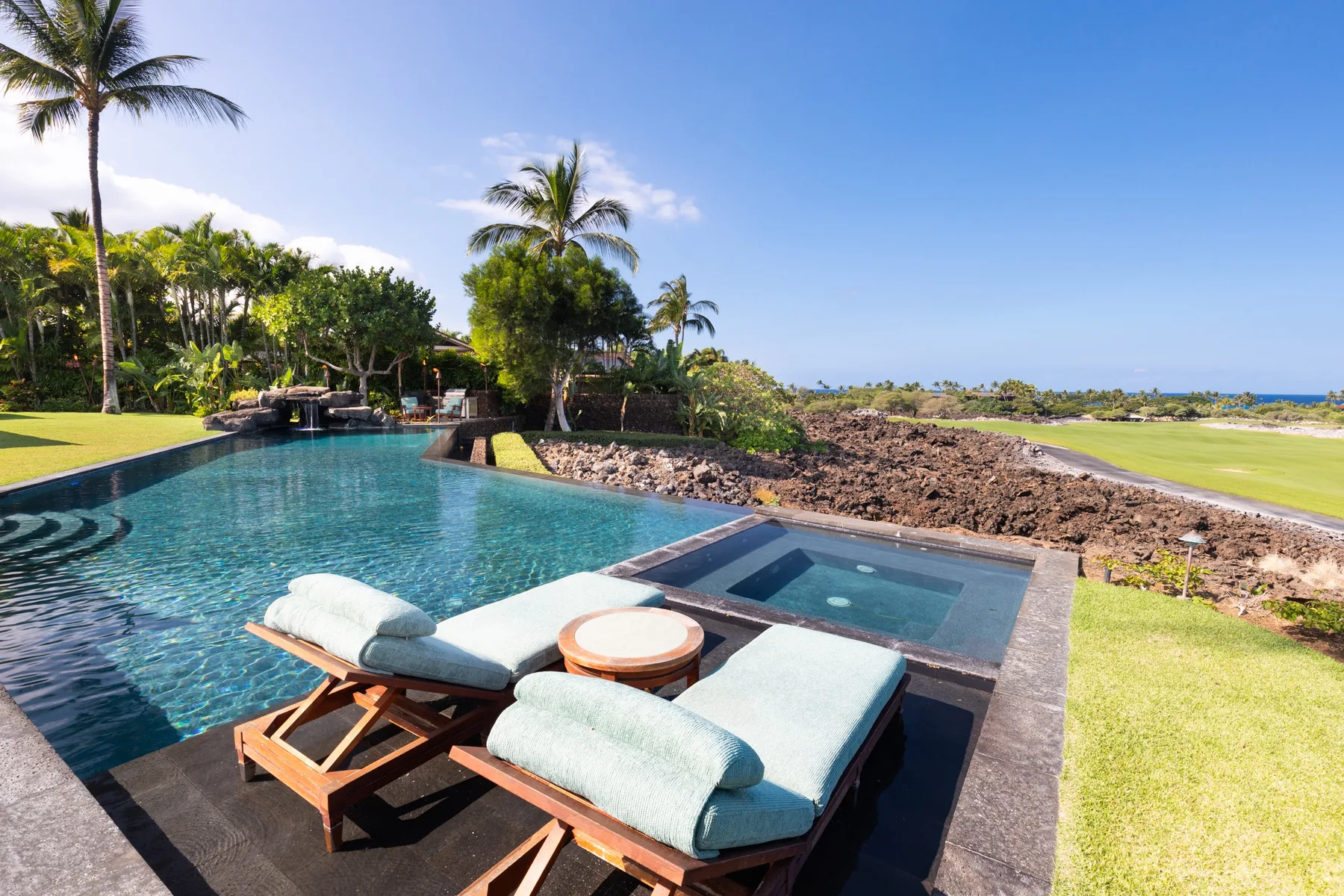 An outdoor pool and lounge area overlook a rocky shoreline and the ocean.
