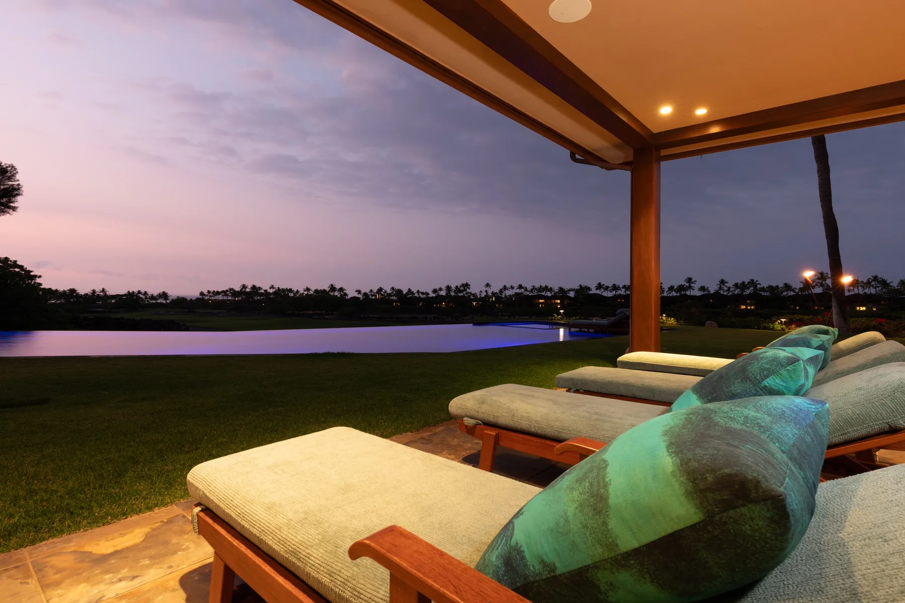 A covered patio seating area overlooks a lawn and water at dusk.
