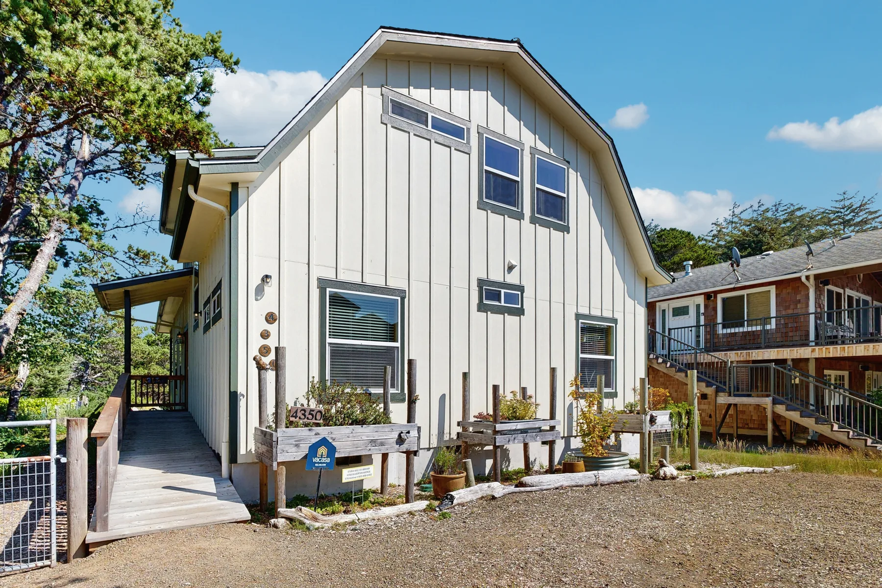 A light-colored house with a raised central roof stands beside a wooden deck.