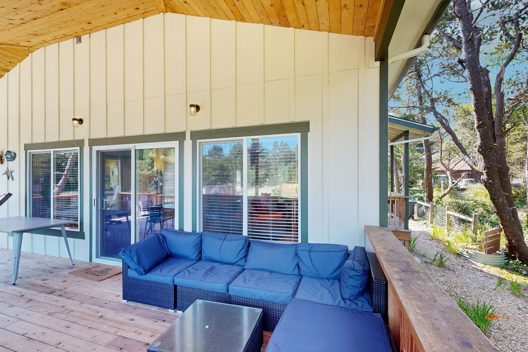 A covered outdoor seating area with a blue couch beside glass doors.