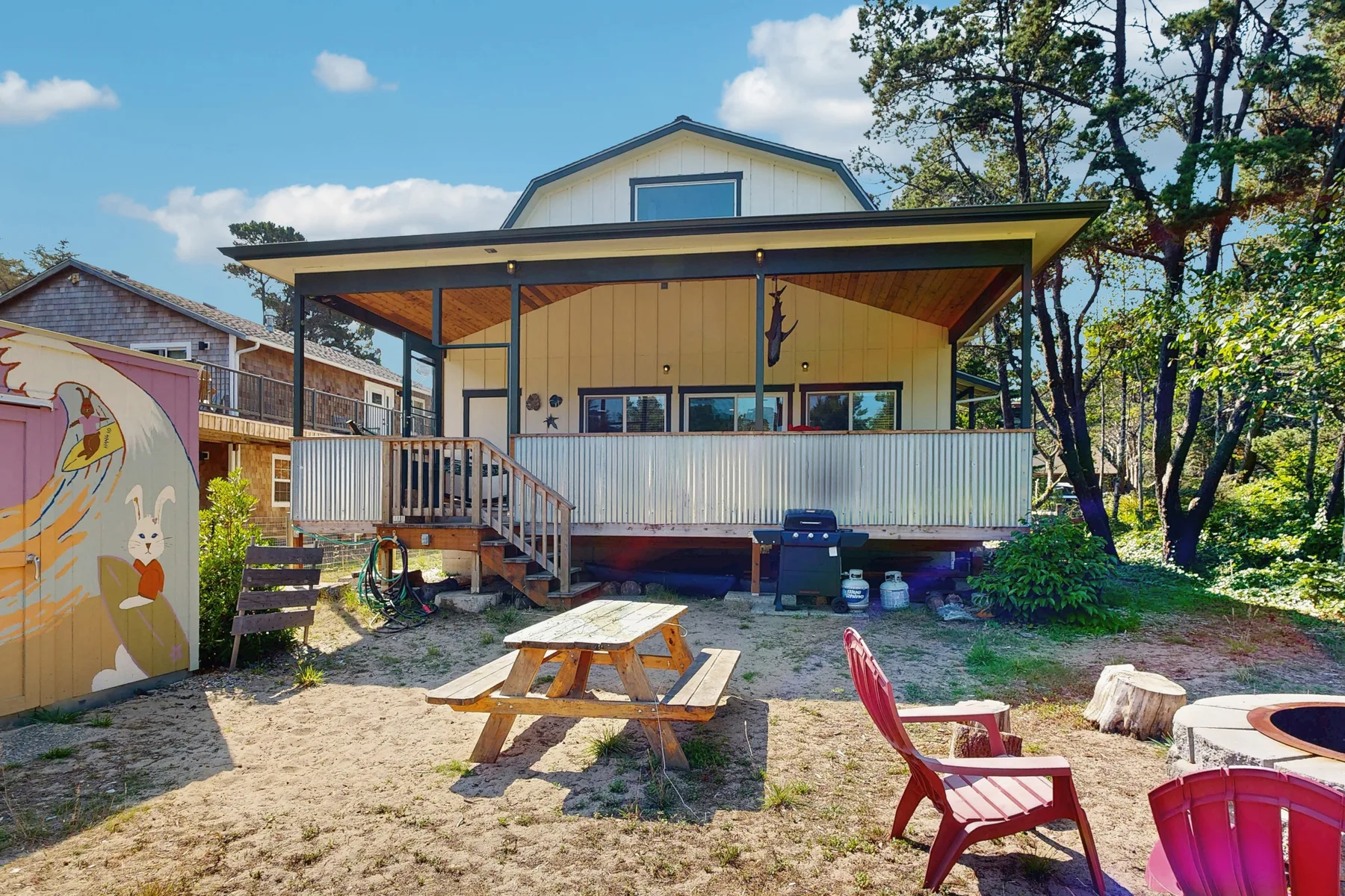 A raised cabin with a covered porch overlooks a sandy outdoor seating area.