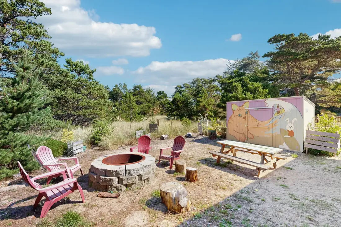 An outdoor seating area with a circular stone fire pit and a painted storage shed.