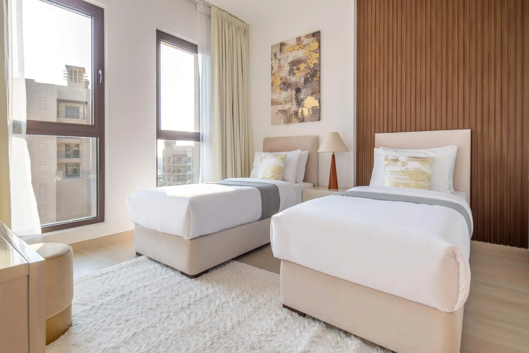 Un dormitorio luminoso con dos camas, ventanas grandes y una pared revestida de madera.