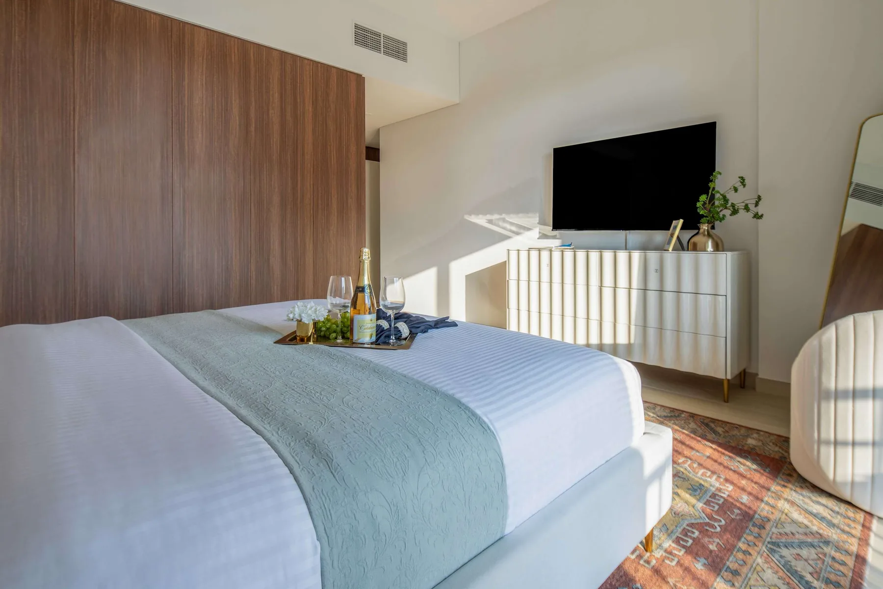 Un dormitorio con una cama tendida y un televisor sobre una cómoda.