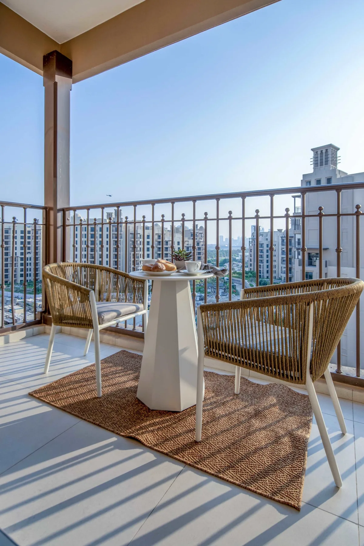 Una zona de estar en el balcón con una mesa pequeña ofrece vistas a edificios cercanos.