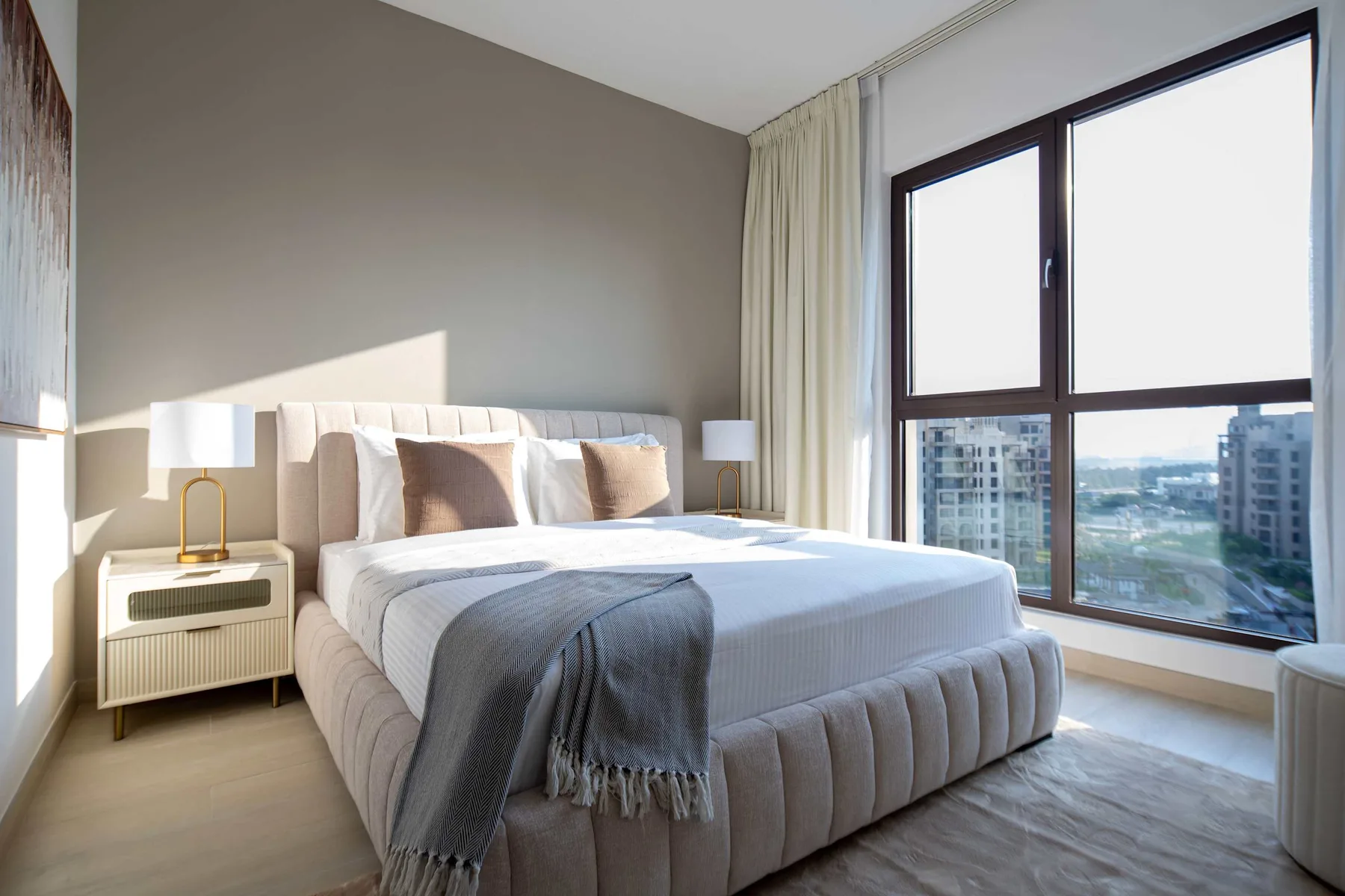 Un dormitorio luminoso con una cama tendida junto a una ventana grande.