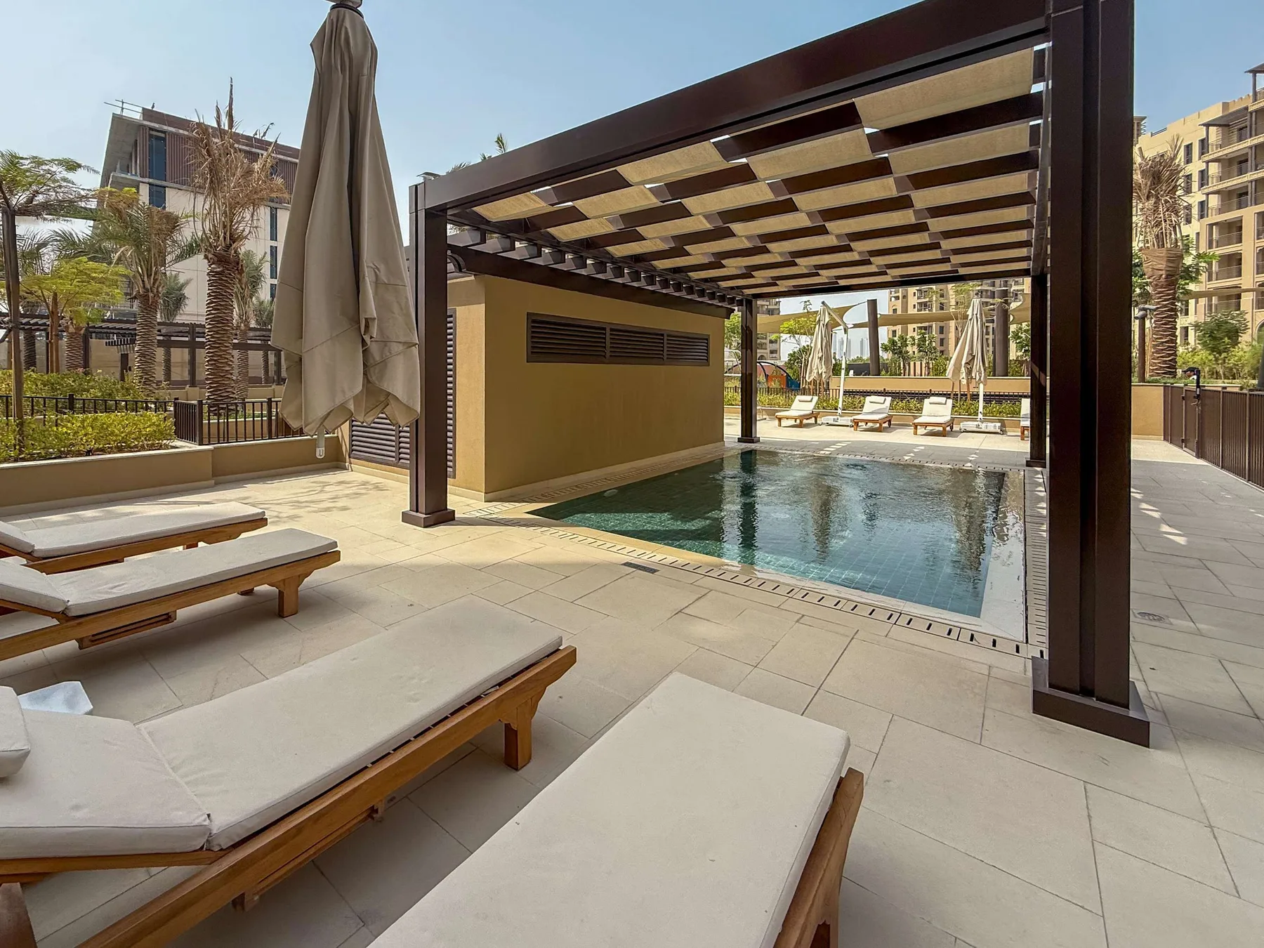 Una piscina al aire libre junto a asientos de descanso bajo una pérgola sombreada.