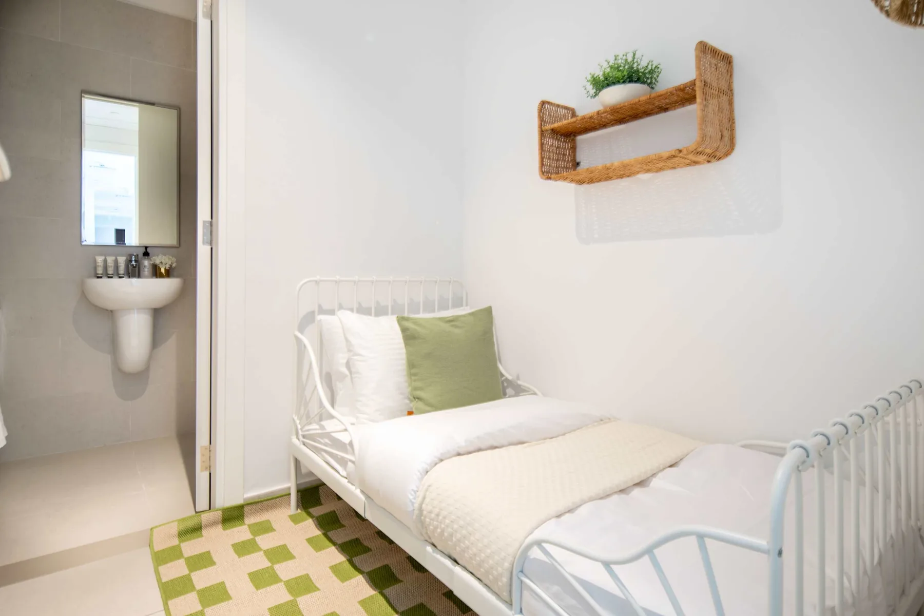 Un dormitorio luminoso con una cama blanca, un cojín verde y un estante de pared.