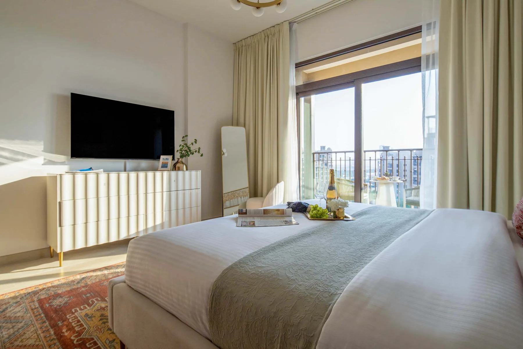 Un dormitorio con una cama bien tendida, un televisor y puertas de vidrio que dan a un balcón.