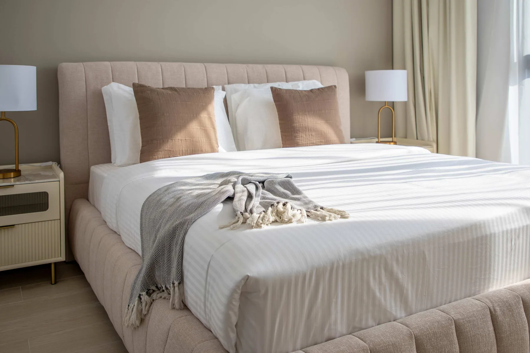 Un dormitorio con una cama bien tendida y cortinas claras.