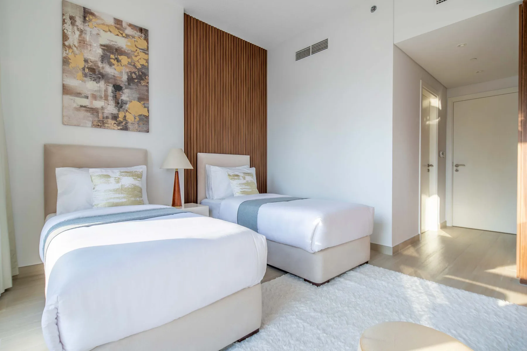 Un dormitorio luminoso con dos camas, ropa de cama blanca y una alfombra.