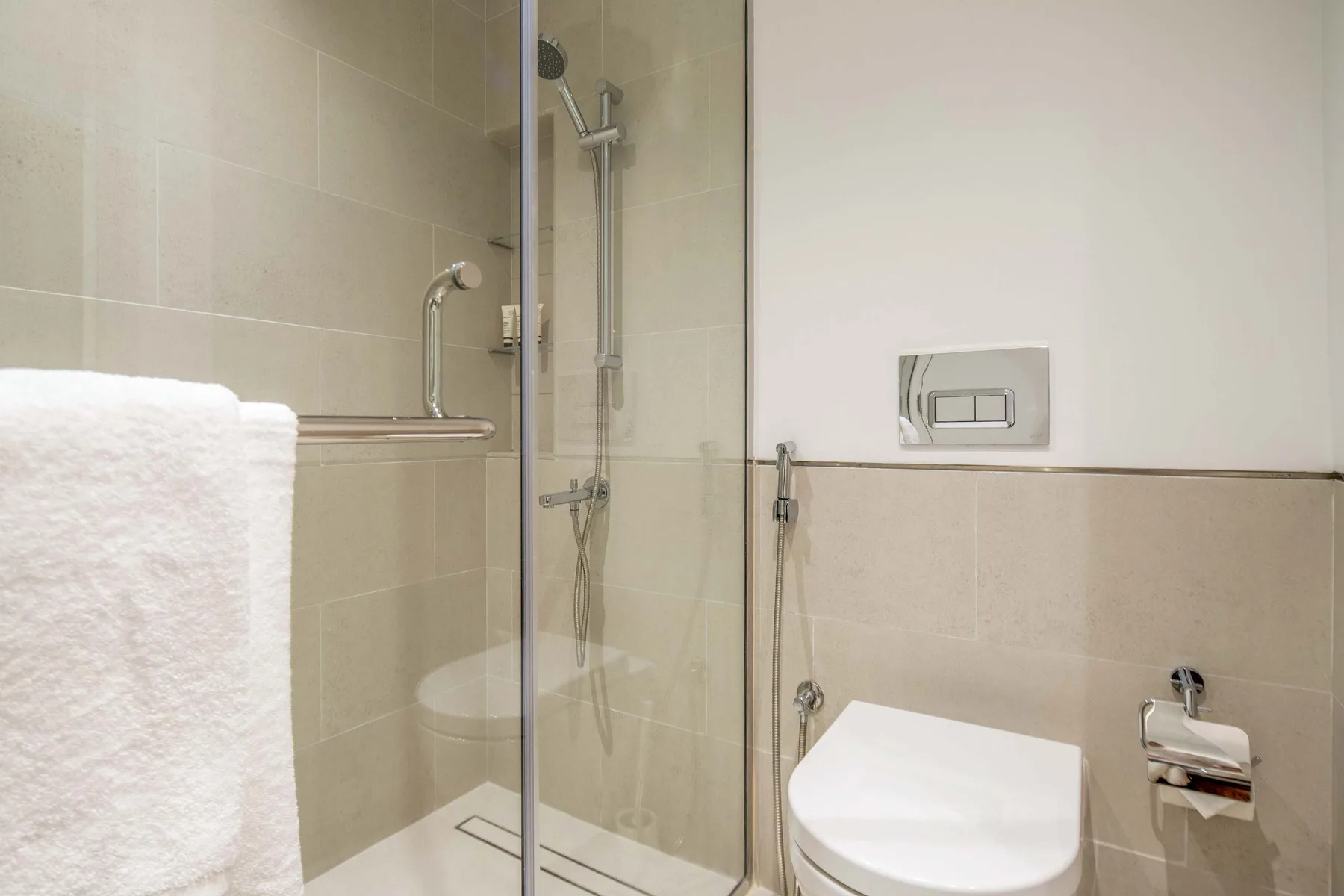 Un baño alicatado con ducha de vidrio e inodoro suspendido.