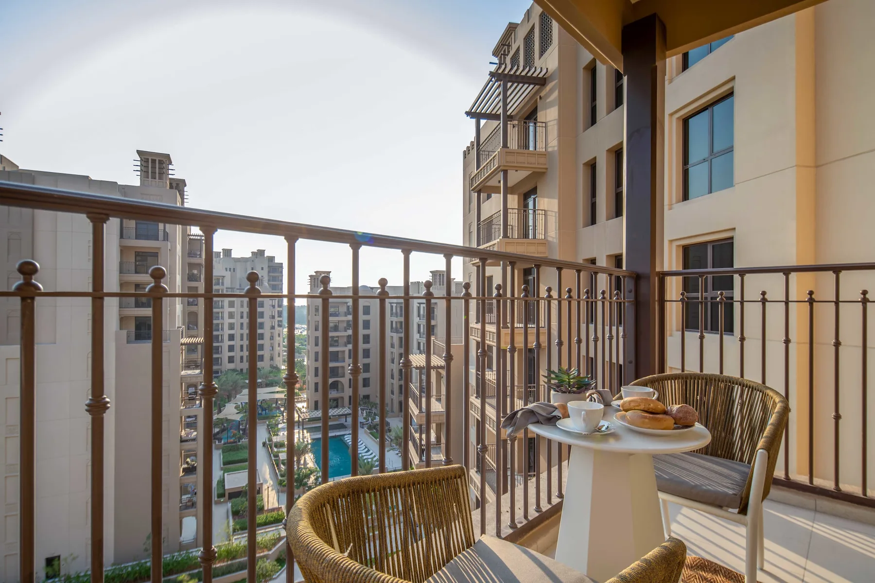Una zona de estar en el balcón da a edificios de apartamentos cercanos y una piscina en el patio.