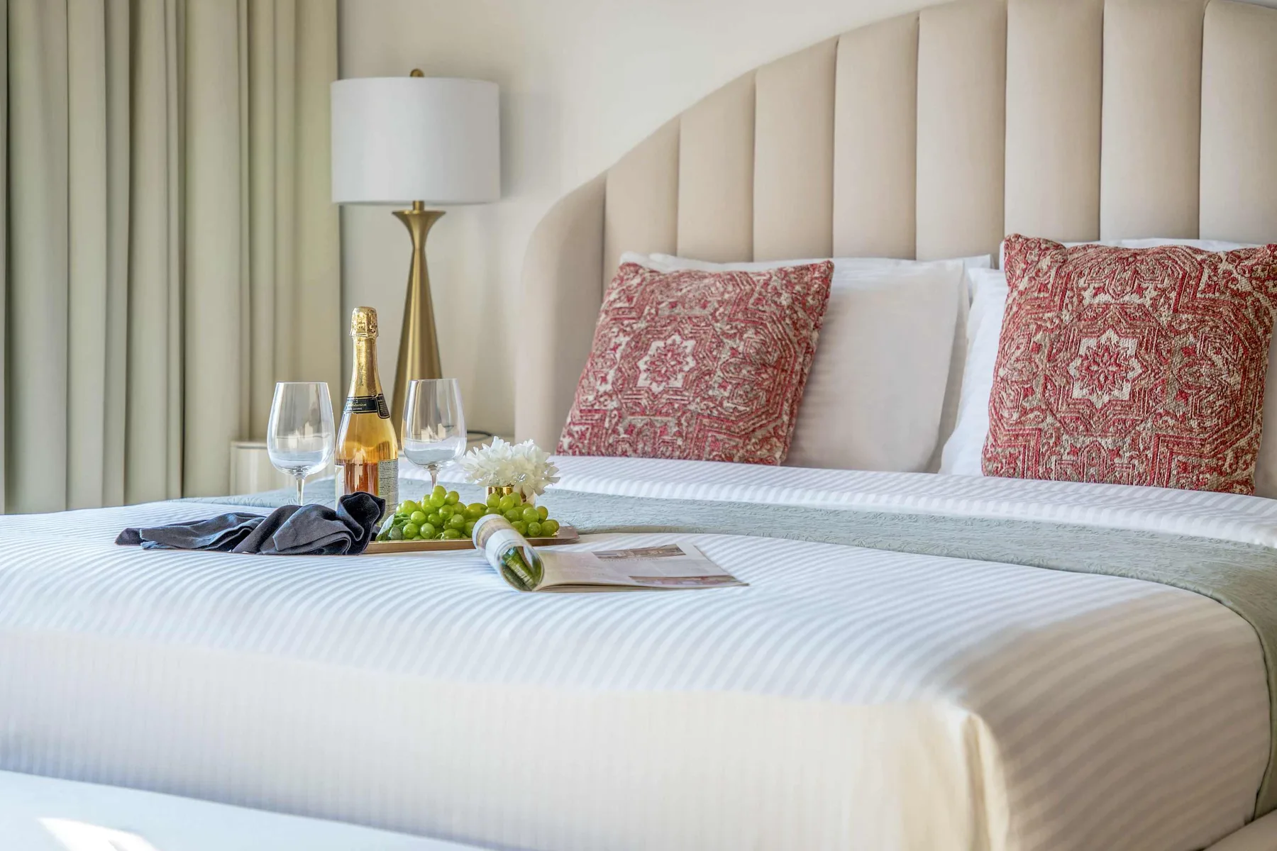 Una cama bien arreglada tiene almohadas estampadas y una pequeña bandeja con bebidas.