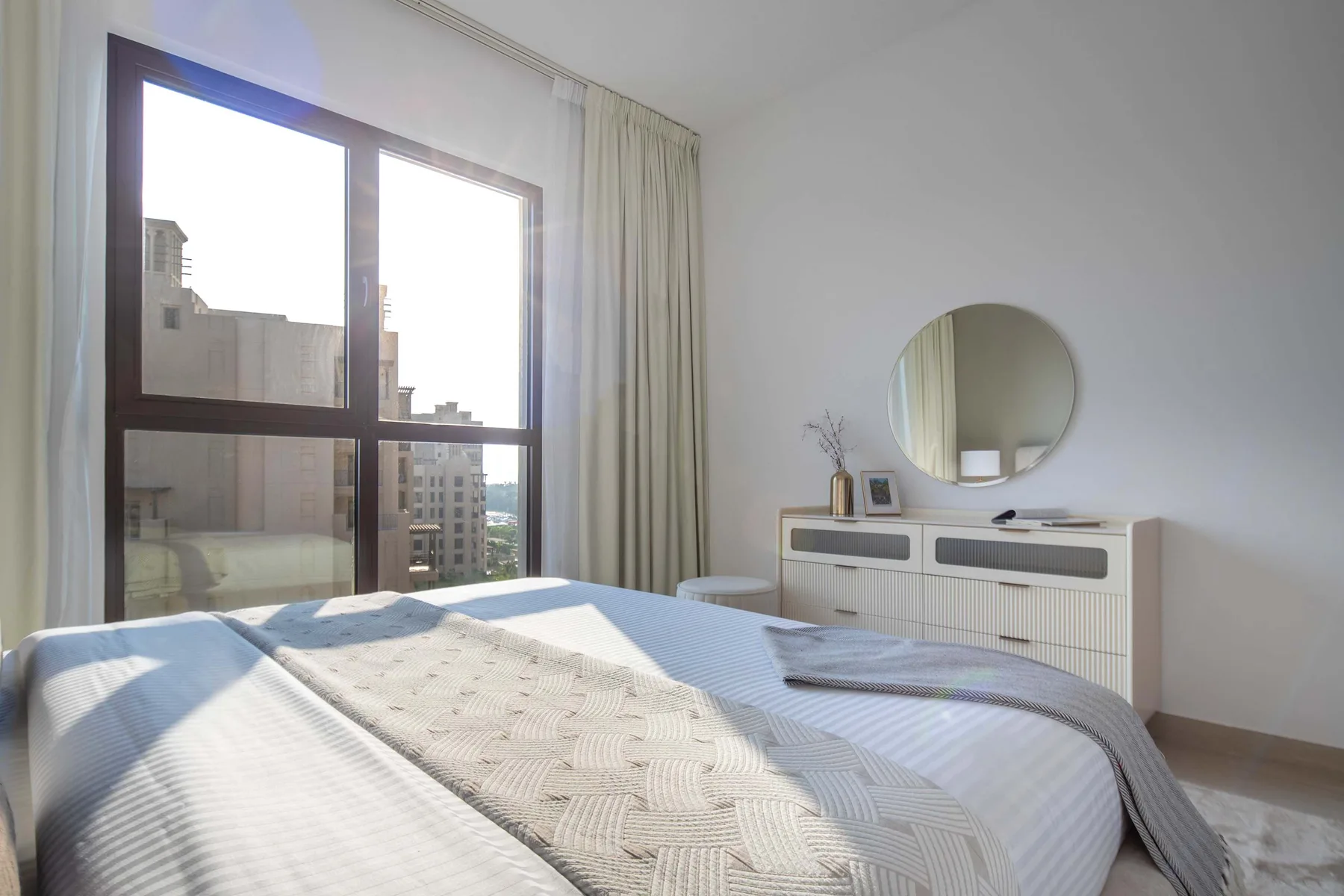 Un dormitorio luminoso con una cama tendida y una ventana grande.