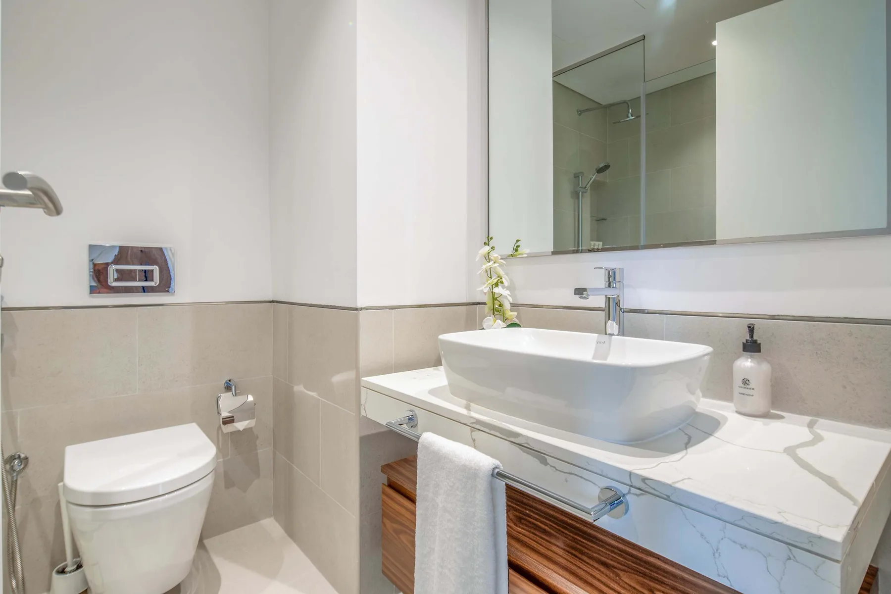 Un baño con lavabo sobre encimera, un espejo grande y una ducha de vidrio.