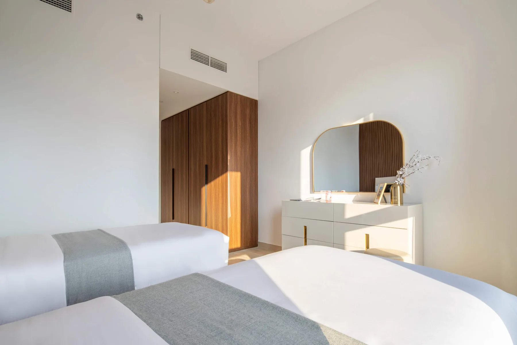 Un dormitorio luminoso con ropa de cama blanca, una cómoda y un espejo de pared.