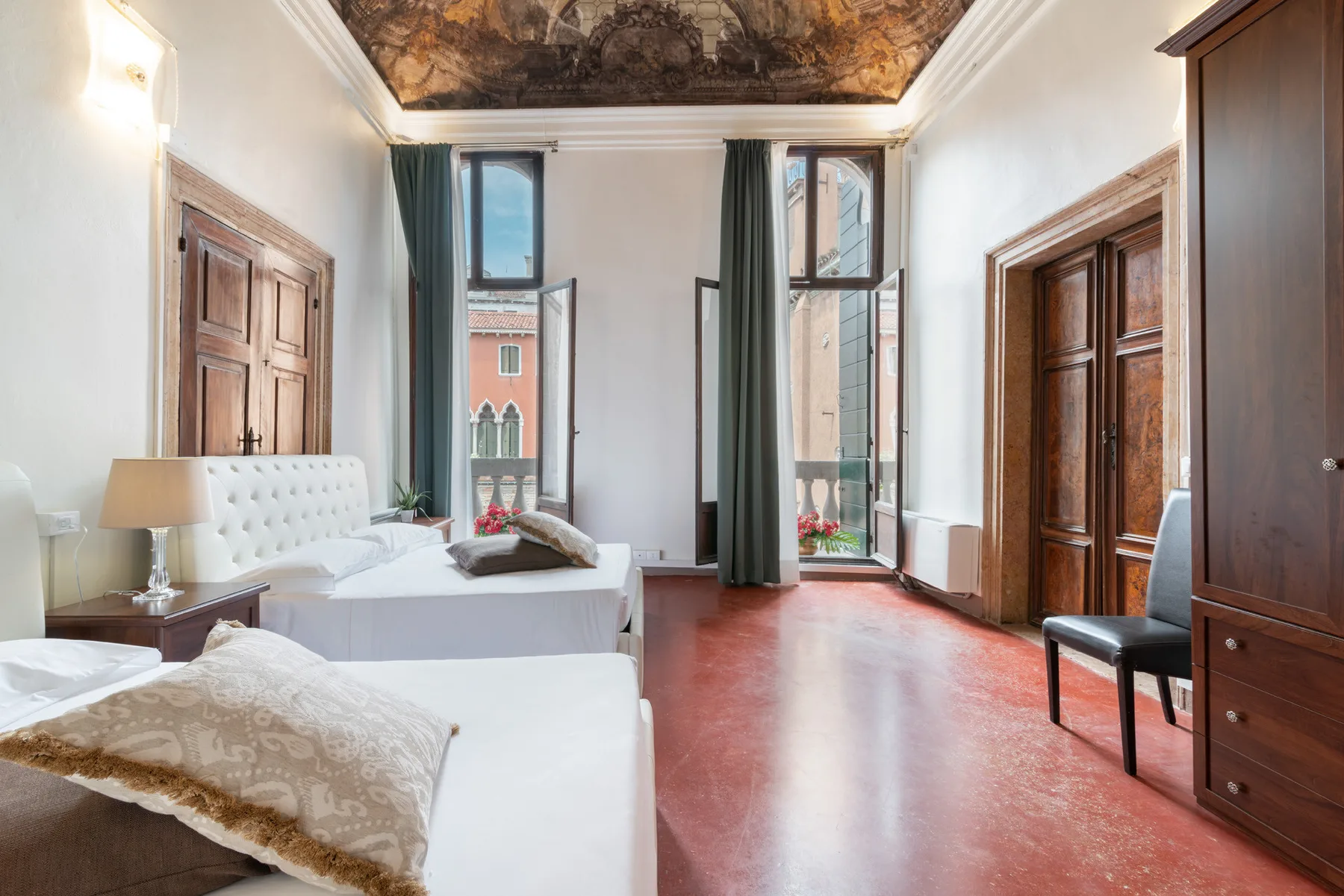 Un dormitorio con dos camas, ventanas altas y muebles de madera oscura.