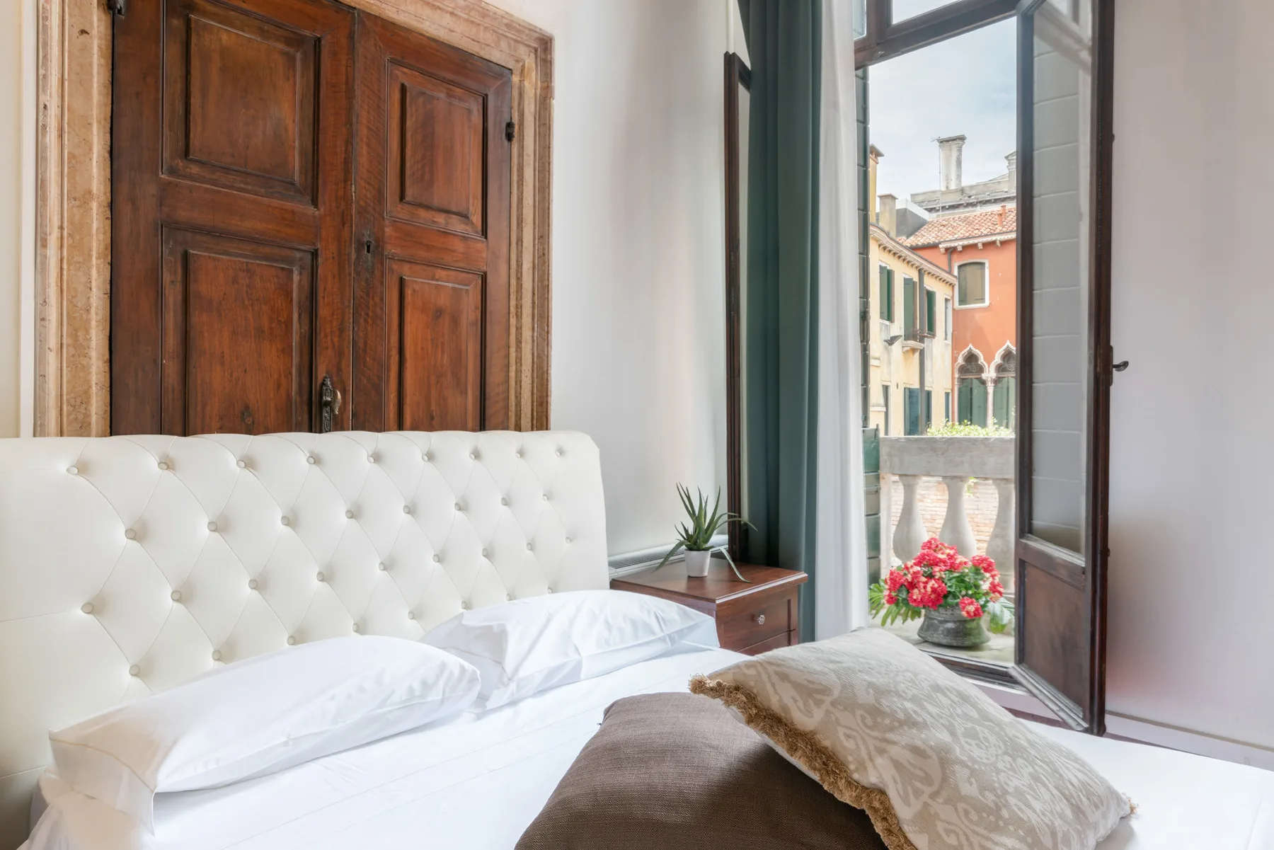 Un dormitorio con una cama junto a una ventana abierta con vistas a edificios coloridos.