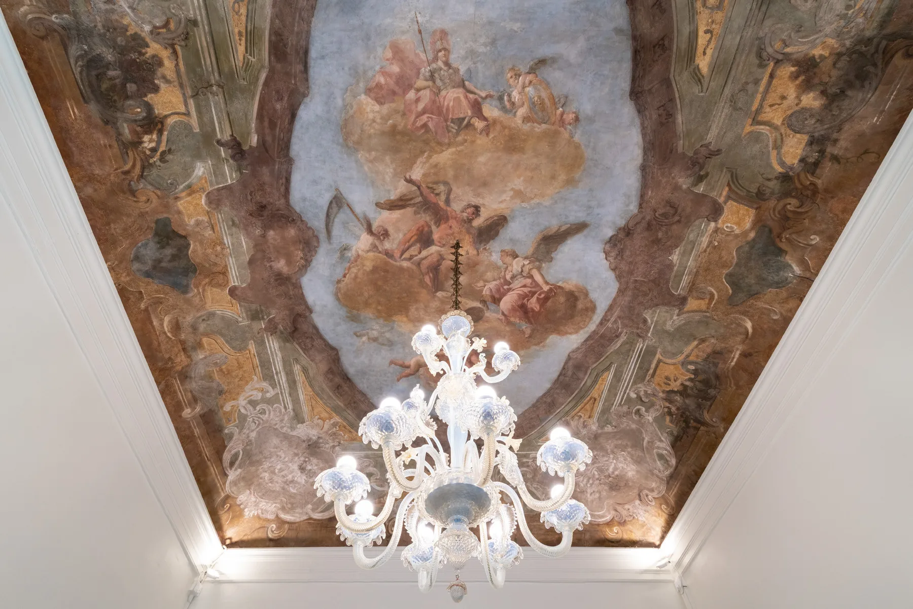Un mural ornamentado en el techo muestra figuras entre nubes sobre una lámpara decorativa.