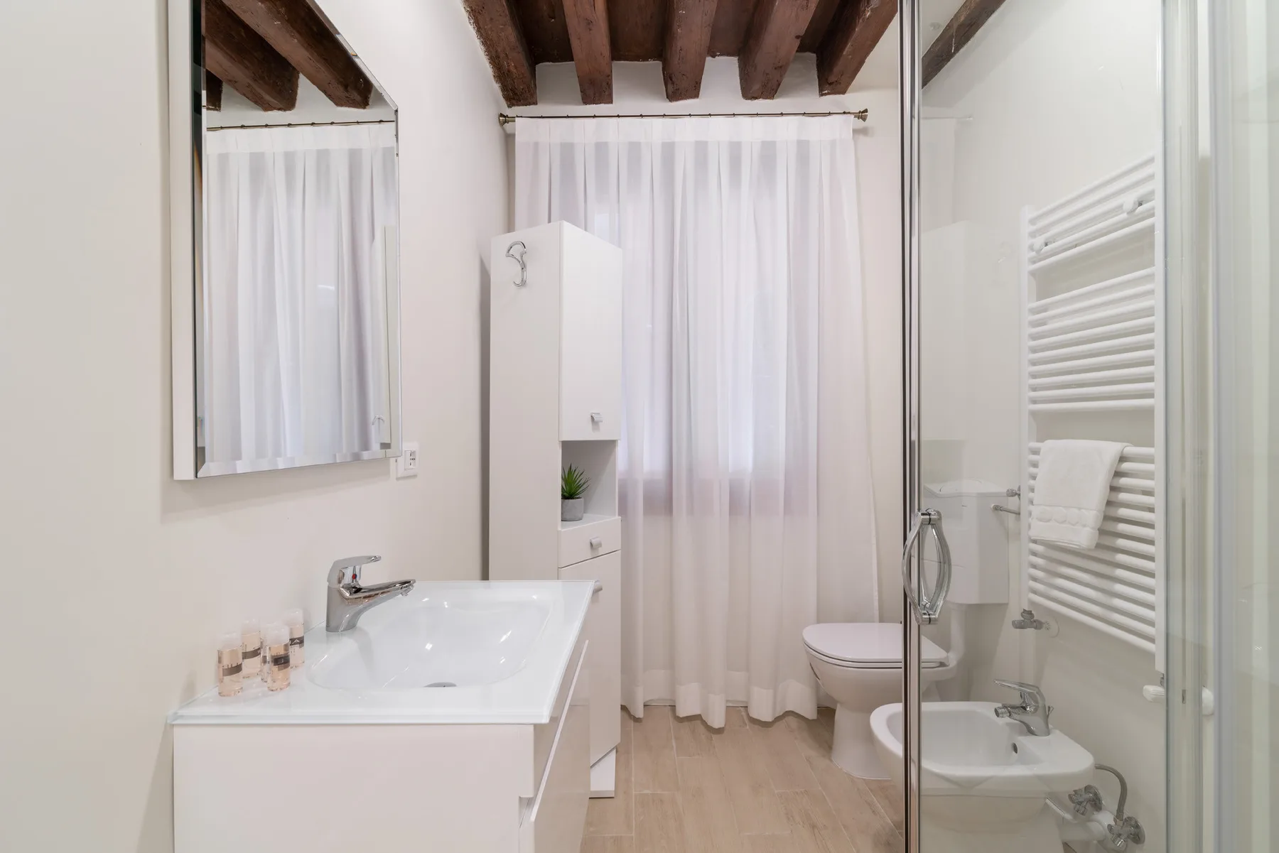 Un baño con lavabo, inodoro, bidé y una ventana con cortina.