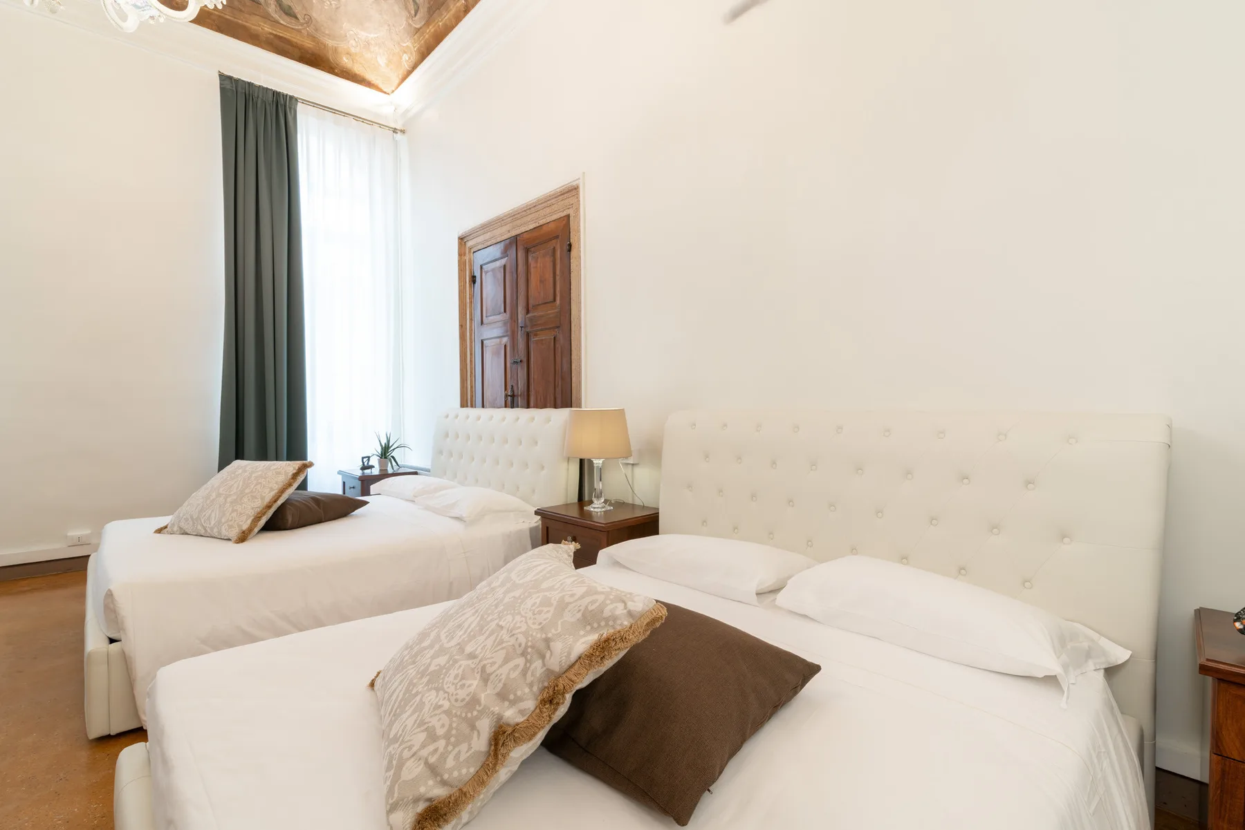 Un dormitorio luminoso con dos camas y una ventana alta con cortinas.