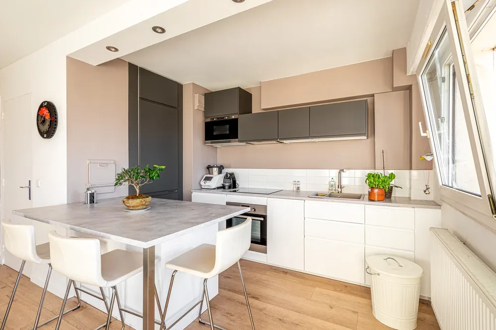 A bright modern kitchen with a countertop, white cabinets, and dining seating.